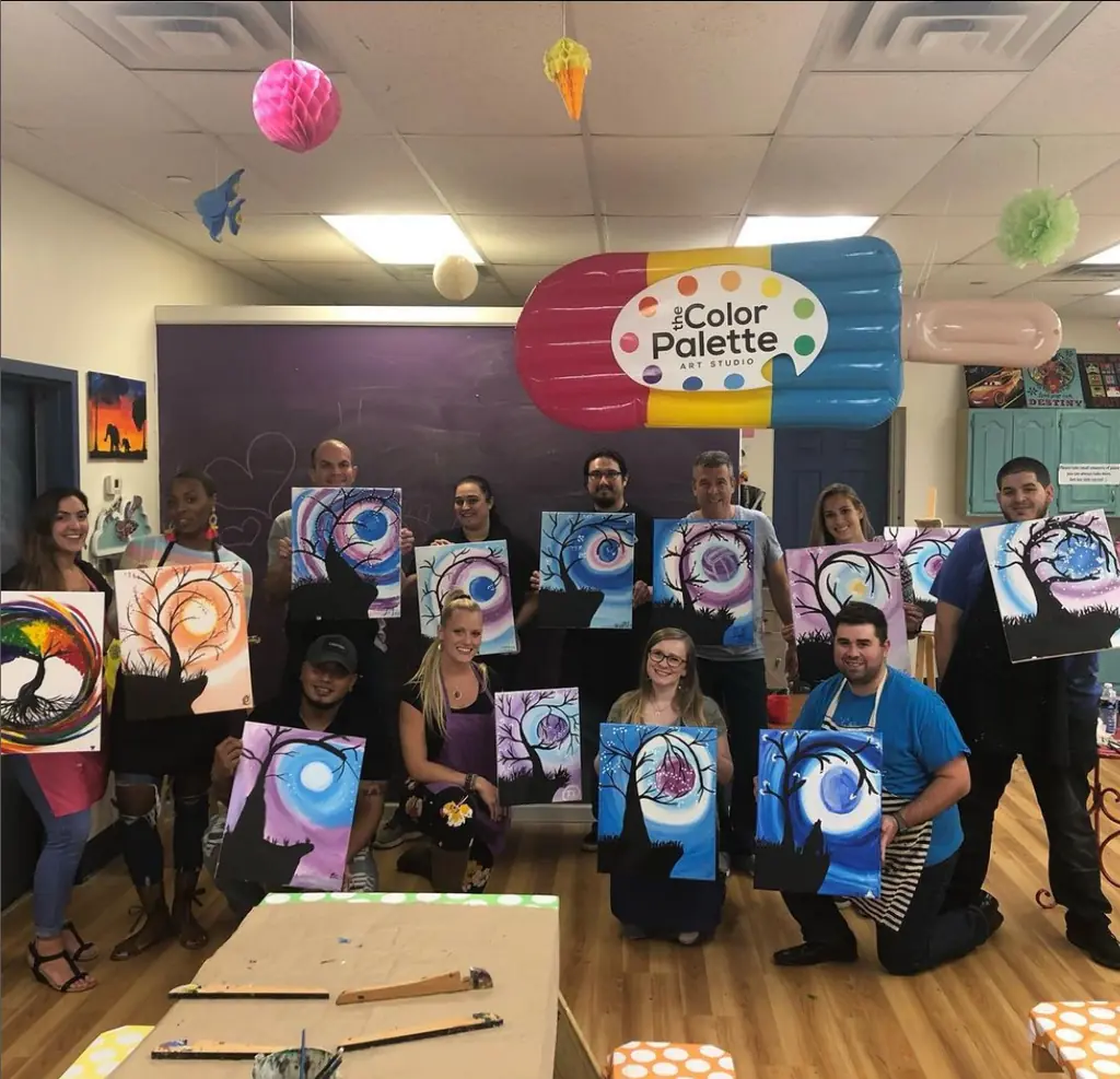 A large group with their finished paintings in front of The Color Palette sign
