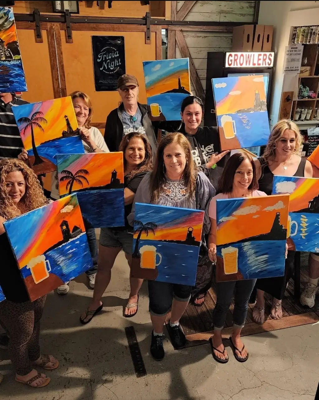 A group of adults proudly holding up their finished sunset paintings