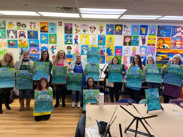 An adult art class holding up their paintings in front of the art wall
