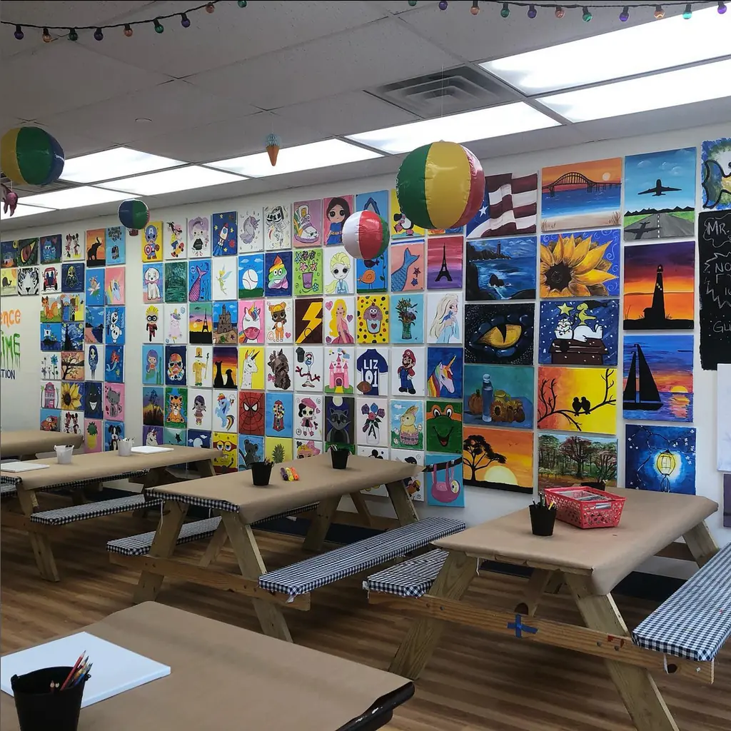 The studio's painting tables in front of a floor-to-ceiling wall of student art